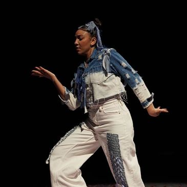 Dancer in patchwork denim outfit performing against black background.