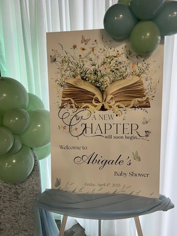 A baby shower sign with an open book and floral design, welcoming guests to Abigale's event.