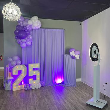 A purple-themed 25th birthday photo setup with balloon decorations and illuminated numbers.