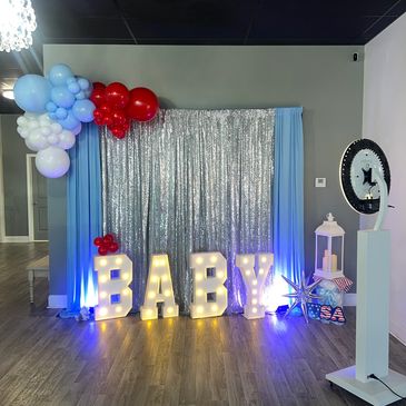 Illuminated BABY sign with balloons and silver backdrop for a baby celebration.