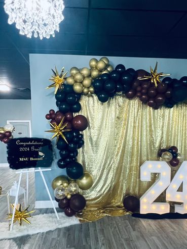 Graduation decor in gold and black with drapes, balloons, and light up marquee numbers.