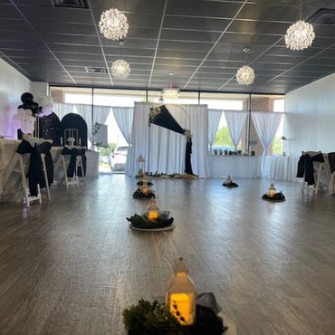 Elegant indoor event setup with white chairs, black bows, and lit lanterns on the floor.