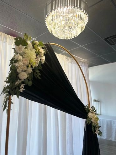 Elegant wedding arch with black fabric and white floral arrangements under a crystal chandelier.