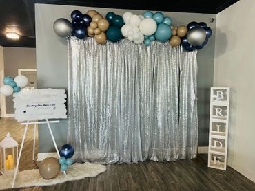 Elegant silver curtain backdrop with balloon garland for a bridal event.