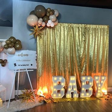 Gold shimmer wall with balloons and light up "BABY" marquee letters for baby shower.