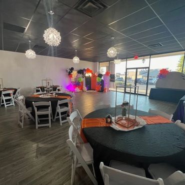 Spacious event room with decorated tables and colorful balloon arch near windows.