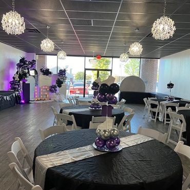 Elegant party room with black and purple balloon decorations and chandeliers.