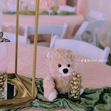 Teddy bear centerpiece with balloons and golden decorations on a party table.