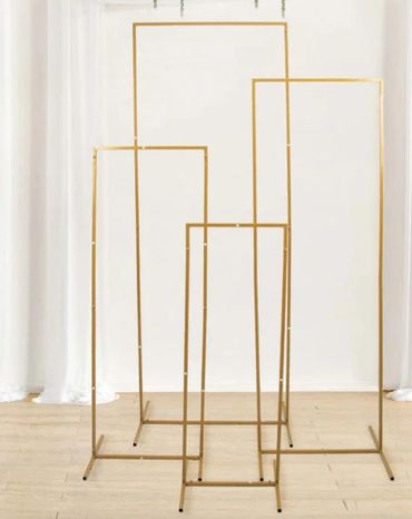 Four gold metal display frames of varying heights on a wooden floor.