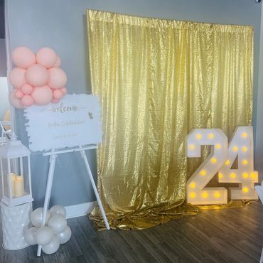 Elegant gold shimmer wall with marquee numbers "24" and custom welcome sign for graduation party.