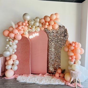 Elegant peach and pearl balloon arch with soft pink and gold backdrops for a celebration.