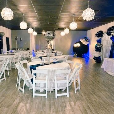 Elegant event hall decorated with white chairs and blue-black balloon arrangements.