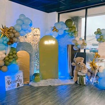 A baby shower setup with blue and gold balloons, teddy bears, and decorative arches.