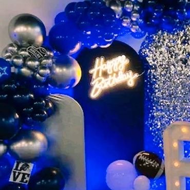 A 65th birthday party setup with blue, silver balloons, and illuminated numbers.