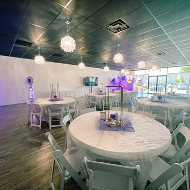 Elegant event space with white tables and purple decorations.