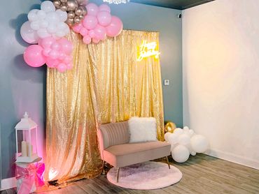 Elegant party setup with gold backdrop, balloons, and plush seating.