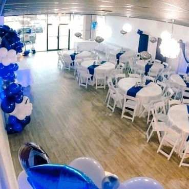 A party room decorated with blue and white balloons and tables with blue runners.