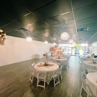 Elegant event space with round tables, white chairs, and gold balloon decorations.