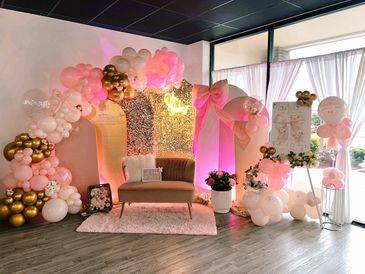 Elegant baby shower setup with pink, white, and gold balloons and cozy seating.