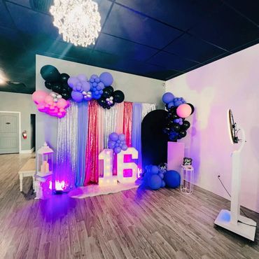 Decorated birthday setup with balloons and illuminated number 16.