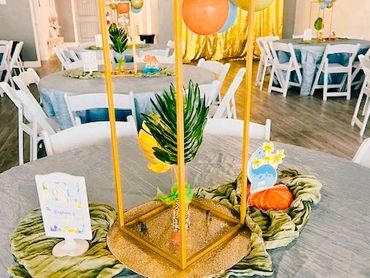 Colorful and tropical-themed table centerpiece with balloons and greenery.
