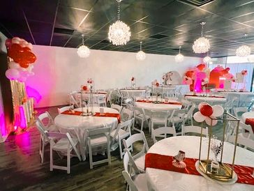 Elegant event setup with white tables, chairs, and red decorations under chandeliers.