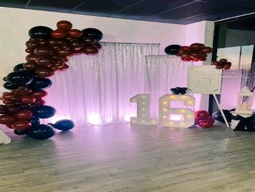 A decorated 16th birthday party setup with balloons and illuminated numbers.