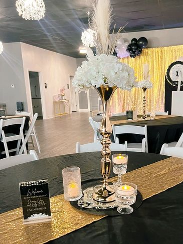 Elegant black and gold engagement party table setting with floral centerpiece and candles.
