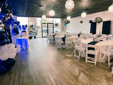 Elegant event space decorated with blue and white balloons and round tables.