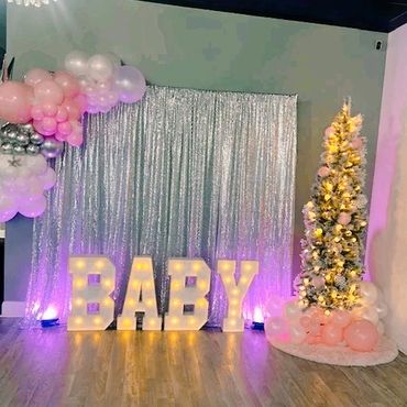 Decorative baby shower setup with illuminated letters and balloon-adorned tree.
