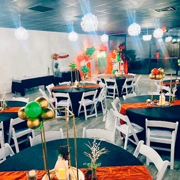 Elegant banquet hall with black and orange table settings and gold-green balloon centerpieces.