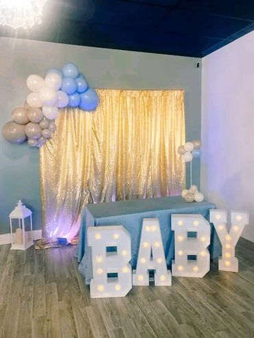 Decorative baby shower setup with balloons and illuminated letters.