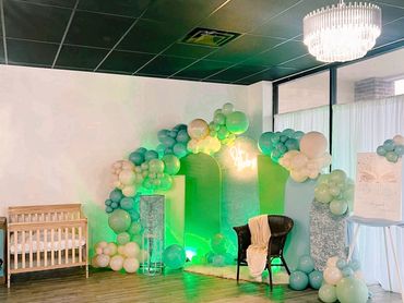 A pastel balloon arch with a chair and crib in a decorated room.