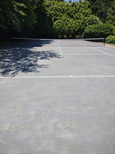 Empty outdoor tennis court surrounded by lush green trees.