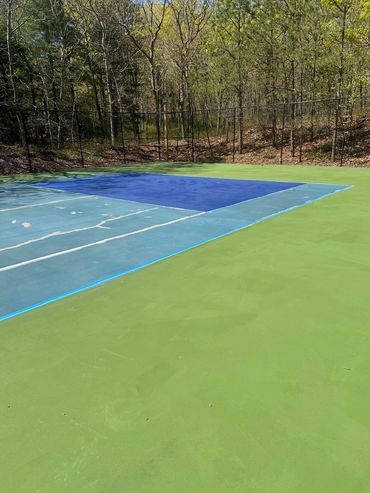 Empty tennis court surrounded by trees under clear sky.