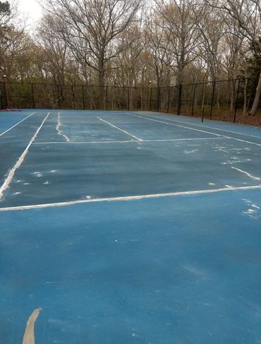 Worn blue tennis court surrounded by trees in late autumn.