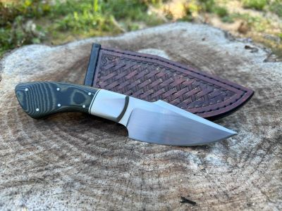 A fixed-blade knife with a patterned handle and sheath on wood.
