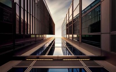 Looking up between two modern glass skyscrapers under a cloudy sky.