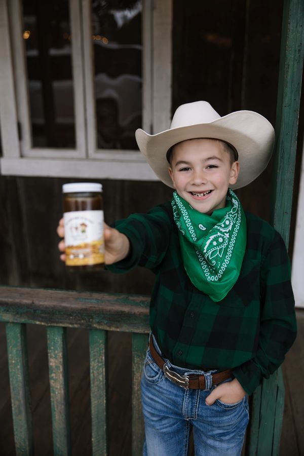 Boy in cowboy hat and bandana holding a jar and smiling.