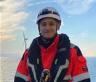 Man in safety gear on a boat with a wind turbine in the background.