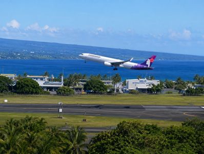 A Hawaiian Airlines plane taking off over a scenic coastal airport.