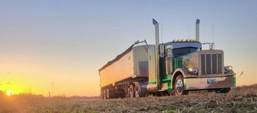 A large semi-truck parked in a field during sunset.