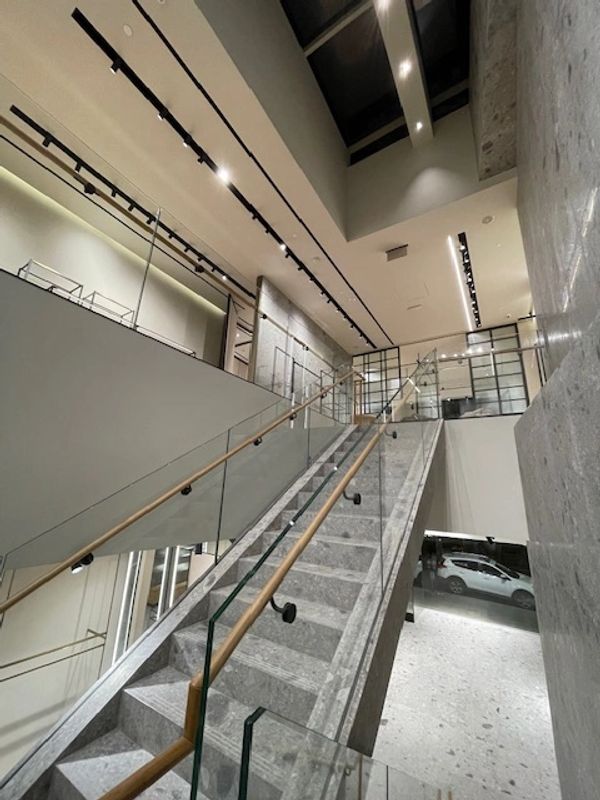 Modern indoor staircase with glass railings and stone steps under bright ceiling lights.