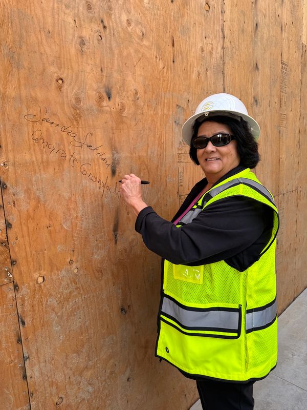 Mujer con casco y chaleco de seguridad firma una pared de madera.