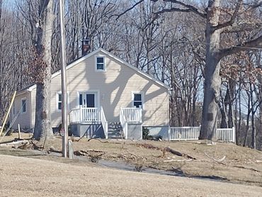 A beige house with white doors and railings surrounded by leafless trees.