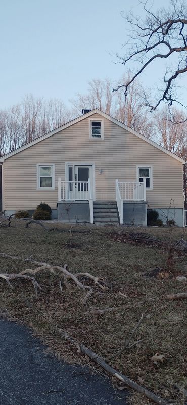 Small beige house with white railings and leafless trees in the background.