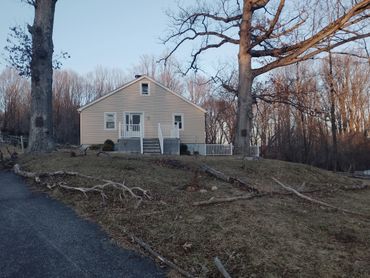 Small beige house with trees and fallen branches in the yard.