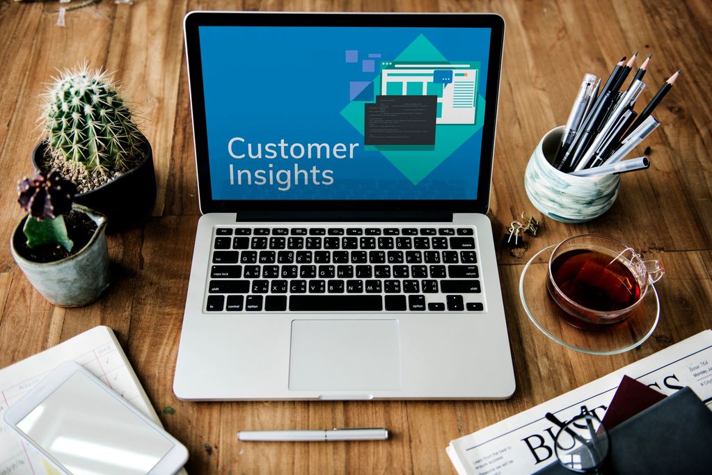 Laptop on wooden desk showing 'Customer Insights' with office supplies around.