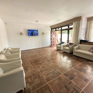 Sala de espera com sofás brancos e TV na parede.