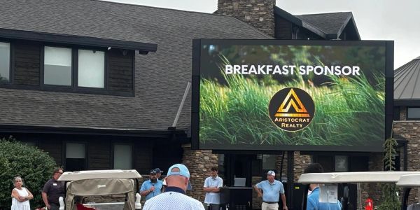 Golfers gather near a sign showing a breakfast sponsor.